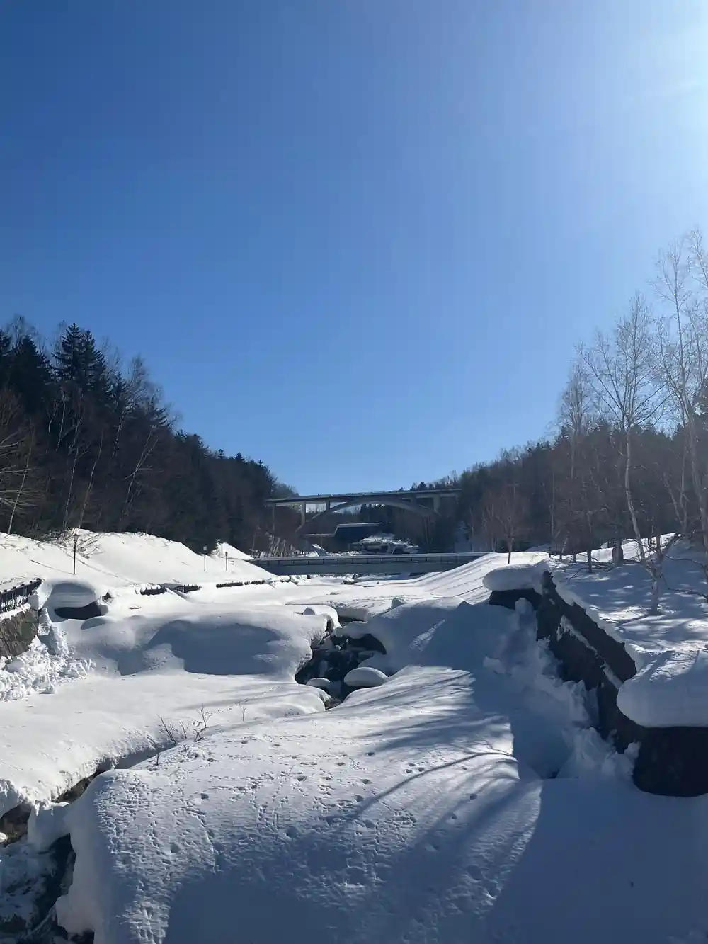 Snowy ground with snow mounds and distant bridge