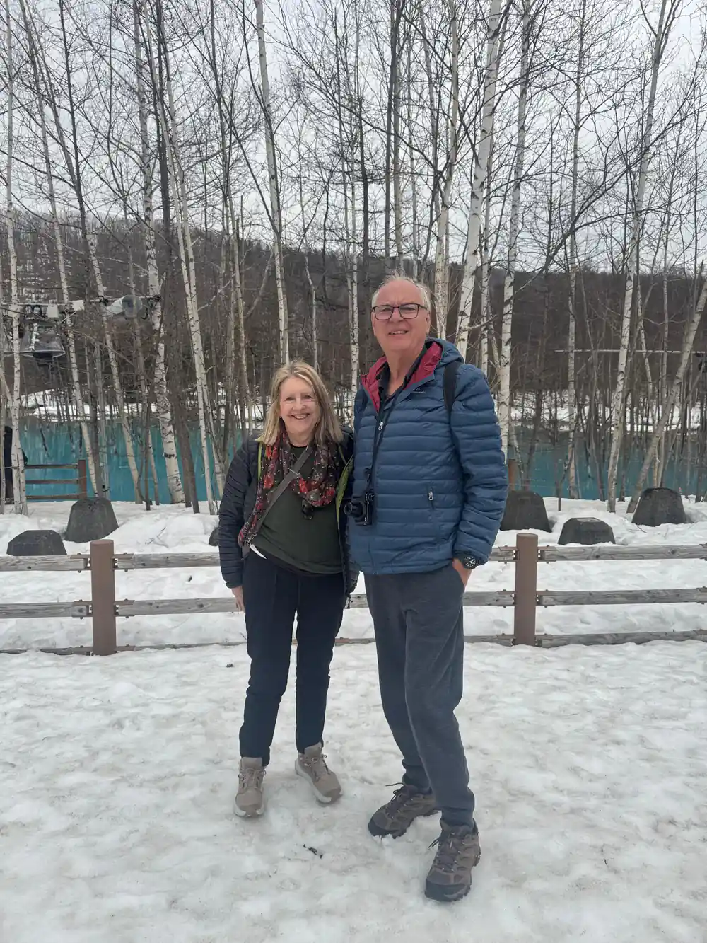 Two people standing on snowy ground with bare birch trees